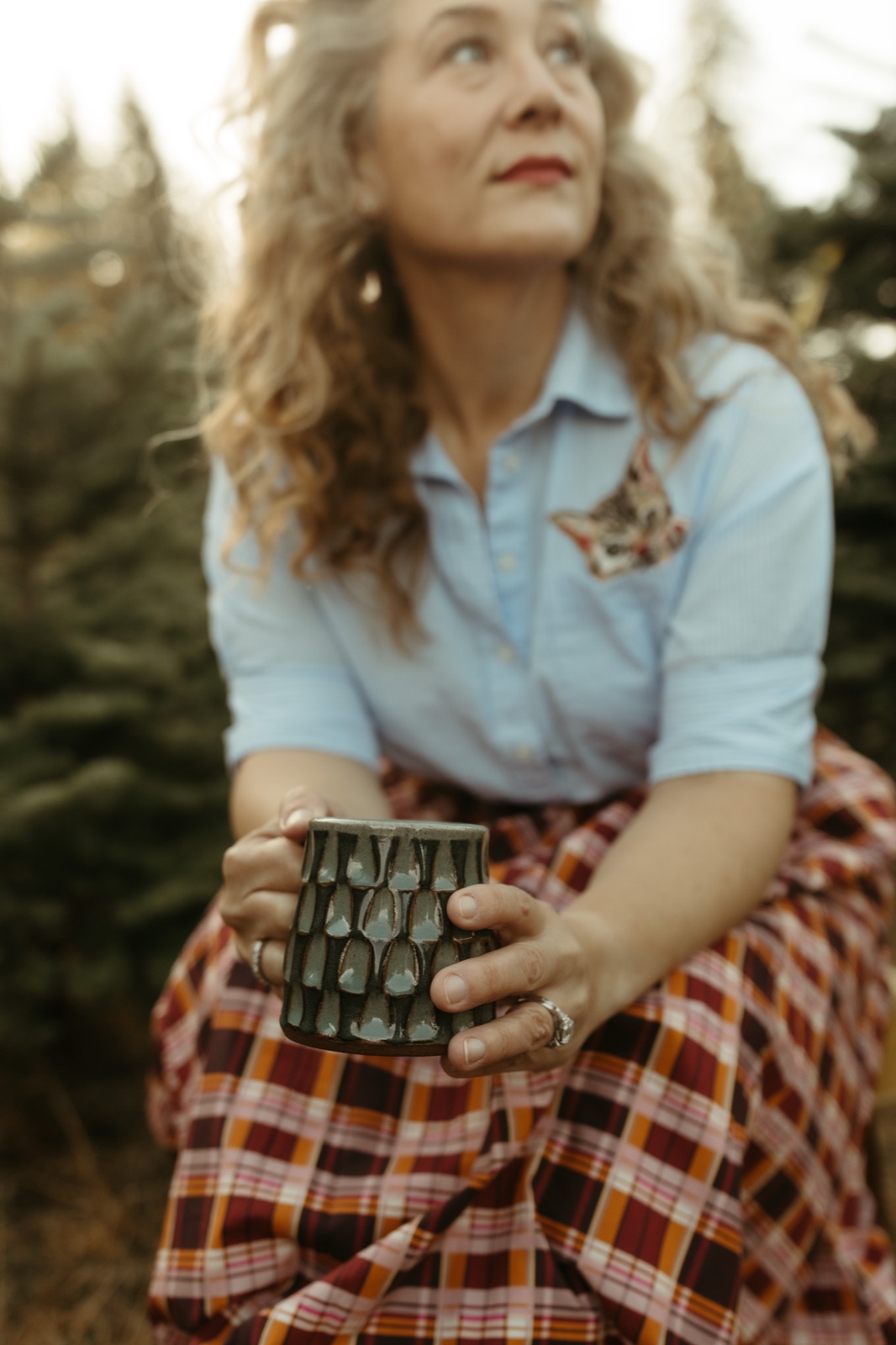 Kat holding a wheel-thrown ceramic mug among Pacific Northwest evergreens